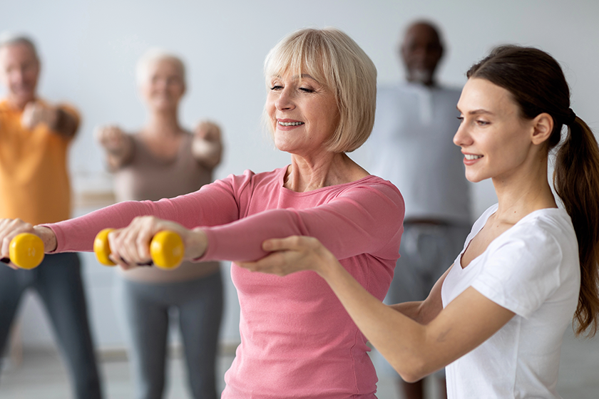Young lady coach helping senior woman while exercising